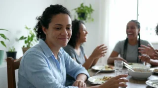 Mulher sorrindo em silêncio na mesa de almoço enquanto a família conversa e ri ao fundo