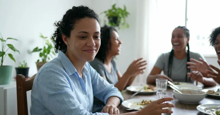 Mulher sorrindo em silêncio na mesa de almoço enquanto a família conversa e ri ao fundo