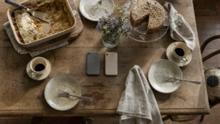 Mesa de almoço de domingo vista de cima, com pratos usados, cafezinhos em lados opostos e dois celulares virados para baixo no centro